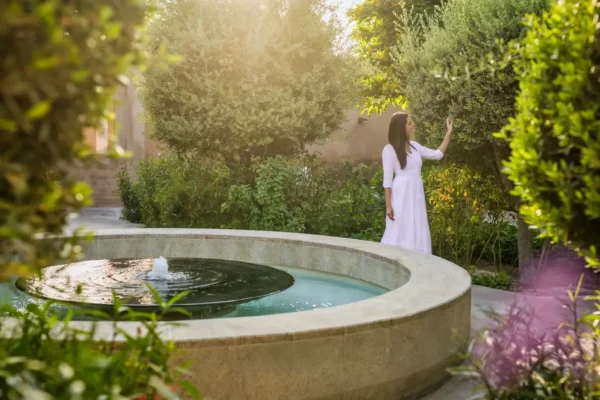 A woman in a white dress gently touching the leaves in the greenery garden of wellness resort.