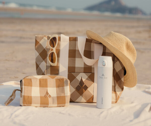 Chiva-Som Collection products on the beach including flask, amenity bag, and tote bag.